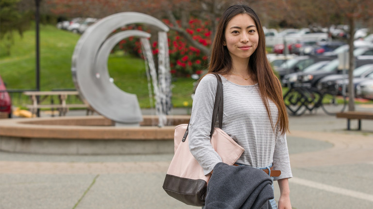 A student stands in front of a large fountain in the shape of the Camosun logo.